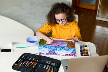 Caucasian teenage girl is drawing sitting at the table. Online education concept.