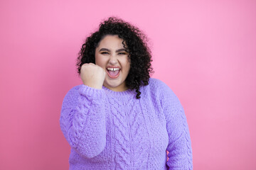 Young beautiful woman wearing casual sweater over isolated pink background angry and mad raising fist frustrated and furious while shouting with anger. Rage and aggressive concept.