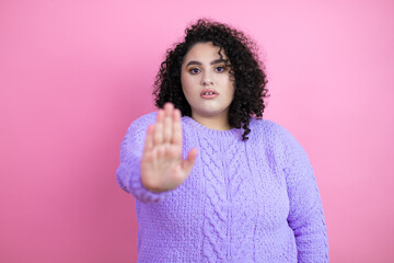 Young beautiful woman wearing casual sweater over isolated pink background serious and doing stop sing with palm of the hand.