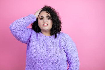 Young beautiful woman wearing casual sweater over isolated pink background putting one hand on her head smiling like she had forgotten something