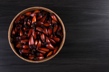 Typical araucaria seeds used as a condiment in Brazilian cuisine in winter. Brazilian pinion nuts in brown and red wooden bowl on gray wooden background