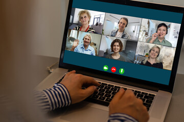 View over businesslady shoulder seated at workplace desk look at computer screen where collage of many diverse people involved at video conference negotiations activity, modern app tech usage concept