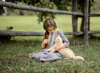 Naklejka premium little girl a girl stroking a cat near a fence in a village in summer