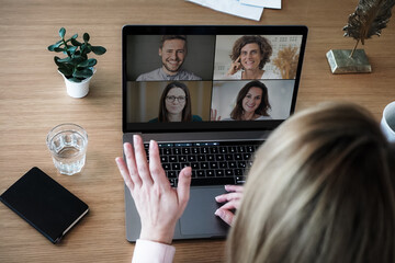 Fototapeta na wymiar remote online working woman on her laptop in home office on a desk while talking, flirting and waving hand in a video chat to greet team in a meeting watching video conference or webinar presentation