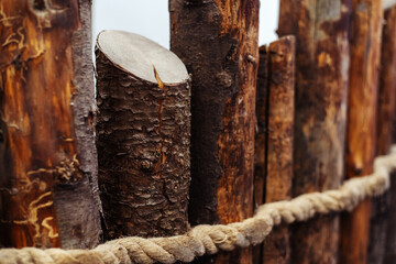 Fragment of a wooden fence made of tree trunks and rope. Close-up
