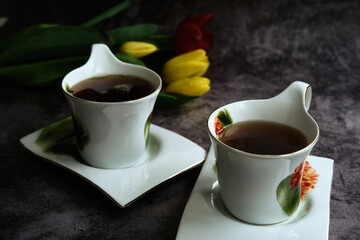 two white cups of tea and yellow and red tulips