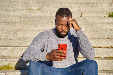 African American man sitting on the stairs looking at his cell phone. Concerned young man. 