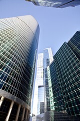 Modern office buildings against bright blue sky. Bottom-up view. Glass facades of tall skyscrapers with bright sun glare and reflections. Economy development, finance and business concept. Downtown.