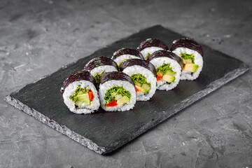 appetizing vegan sushi roll futomaki with pepper cucumber and avocado salad on a black stone plate