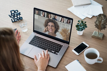 laptop on a work desk showing back view of a woman watching screen of a video conference, a...