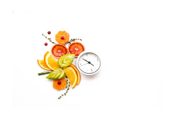 Composition of fresh citrus fruits and a clock (alarm clock) on a white background. Diet and nutrition concept