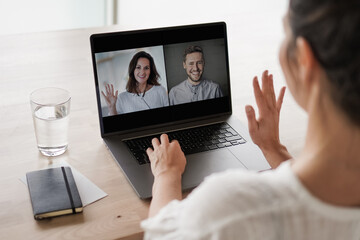 
remote online working woman on her laptop in home office on a desk while talking, flirting and waving hand in a video chat to greet team in a meeting watching video conference or webinar presentation