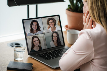 back of a remote online coaching woman sitting on her work desk infront of laptop screen at her home office joining a team meeting or women circle of 4, coaching event or watching video conference