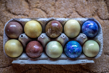 Blue, yellow and brown Easter eggs are in the egg box. The box is lying on a wooden chair on a beige carpet.