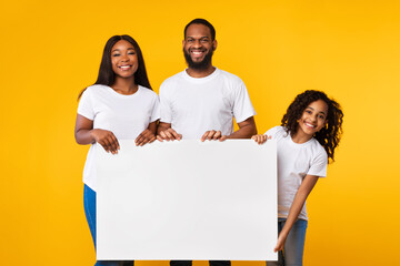 Black family holding blank white advertising billboard at studio