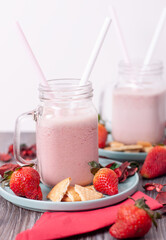 Concepto de algunos batidos de fresa y galletas en jarras sobre platos de color turquesa con trozos de galleta y algunas fresas alrededor de las jarras.