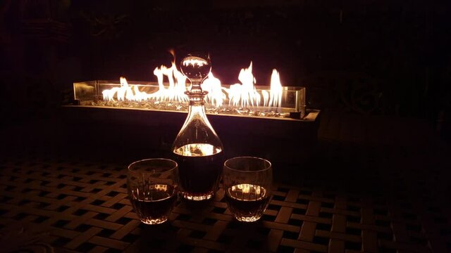Decanter and two glasses in front of rectangular fire pit at night 4K.