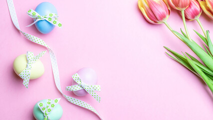 Easter border. Colorful egg with tape ribbon, spring tulips, feathers on pastel pink background in Happy Easter decoration. Flat lay, top view.