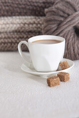 White coffee cup on the background of knitted things. Pieces of cane sugar. Free space. Hobby concept. Vertical photo.