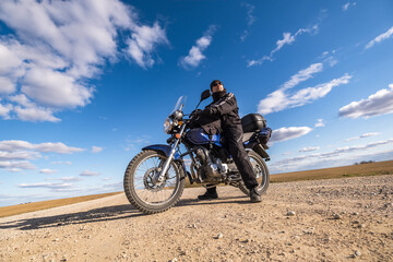 Fototapeta na wymiar man in a black uniform on bike against the backdrop of panorama of field and blue sky. motorcycle travel concept