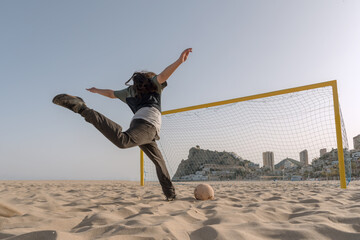 Teenage boy shoots the ball with all his might while playing on the beach. Sports.