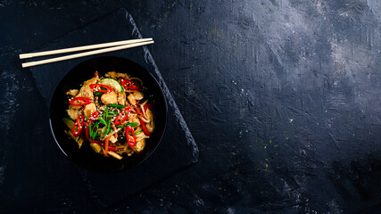 Udon stir fry noodles with chicken and vegetables on black background. hot wok with chicken...