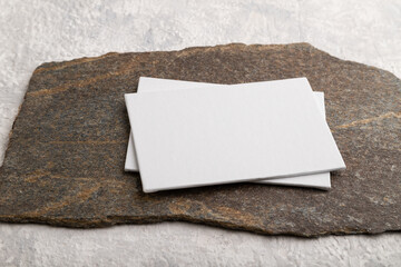 White paper business card, mockup with stone on gray concrete background. canvas, side view, copy space.