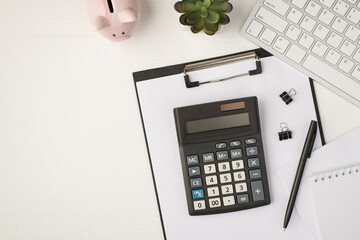 Top view photo of business workplace with keyboard piggy bank plant pen binders notebook papers and calculator on folder on isolated white background with copyspace - obrazy, fototapety, plakaty