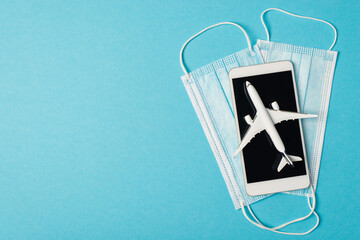 Overhead photo of smartphone face mask and airplane isolated on the blue background with empty space
