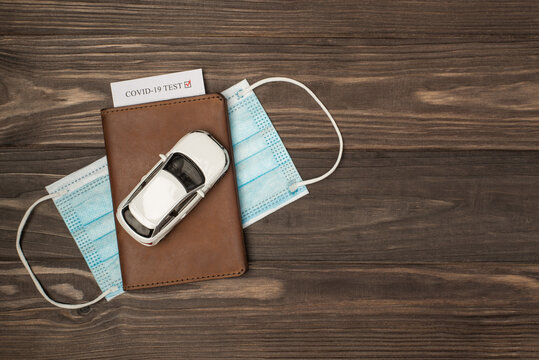 Top view photo of car model on leather passport cover with covid test and medical face mask on isolated wooden table background with copyspace