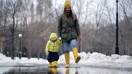 Mom and daughter walking in a puddle in yellow rubber boots