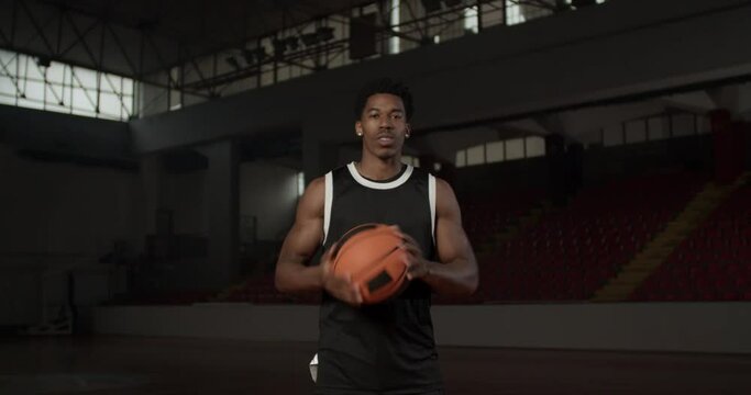 Video portrait of a basketball player bouncing a ball. African american man in uniform posing inside sports hall