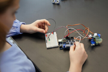 High angle close up of child experimenting with electric circuits while building robots during engineering class in development school