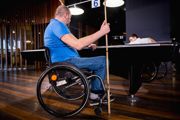 Adult men with disabilities in a wheelchair play billiards in the club