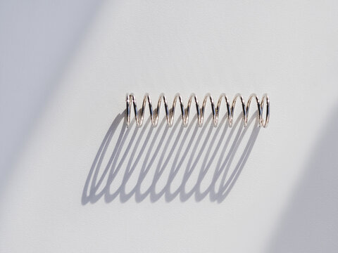 Metal mainspring on white background. Flexible chrome tube. Corrugated object on geometrical banner with copy space on hard sunlight and shadow.