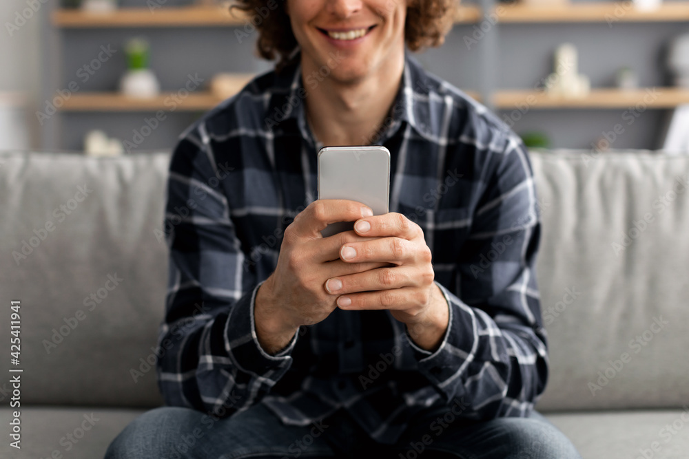 Poster unrecognizable guy using mobile phone sitting on sofa indoor, cropped