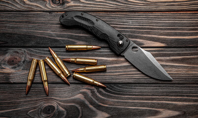 Pocket folding knife and a few rifle cartridges on a wooden back