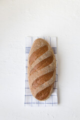 Whole grain rye loaf bread is wrapped lies on a half chick on a light background, fresh hot baked goods, minimalism
