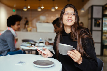 Female student using smartphone while sitting in cafe