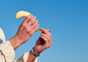 A closeup of a Caucasian man from Spain peeling a ripe yellow banana on clear sky background