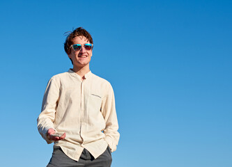 A vertical shot of a Caucasian man holding his phone, smiling and looking forward on sky background