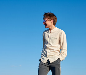 A Caucasian white man with his hands in his pocket looking to the side and smiling on sky background