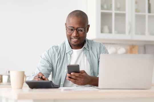 Savings and finances concept. Mature black man using calculator, phone and laptop computer