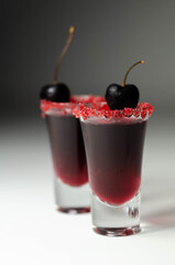 Ruby red cocktail based on vodka, cherry liqueur and syrup in drink shot glass, decorated with fresh cherry and red sugar