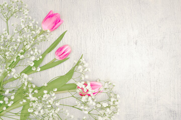 THREE PINK TULIPS WITH GYPSOPHILA ON A WOODEN BACKGROUND