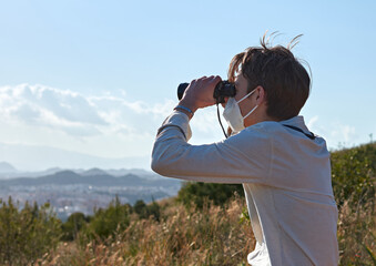Obraz premium A shallow focus shot of a young man from Spain in a white shirt looking over a city through binoculars during the pandemic