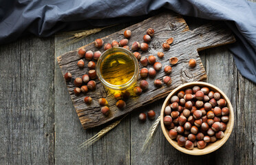 Hazelnut oil, filbert and cooking oil in glass of jar on wooden backdrop, heap or stack of hazelnuts, healty food