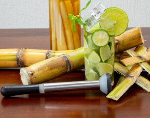 Typical Brazilian caipirinha with cachaça bottle with pieces of sugar cane in sugar cane peels and lemon squeezer, in fine details
