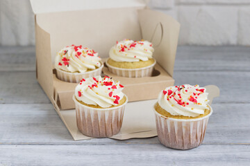 Delicious cupcakes with white cream sprinkled with hearts in a box for cakes.
