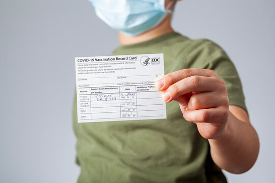 04-02-2021 Clarksburg, MD, USA: It is expected that kids will be getting vaccines before the start of the school year. Concept image showing  a kid holding a COVID-19 vaccination record card